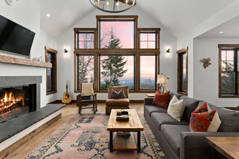 Picture of the great room sitting area with gray couch, wood coffee table rocking chairs and large windows with lake and mountain views.